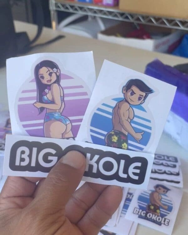 A person holding up two stickers with the words big kole on them.